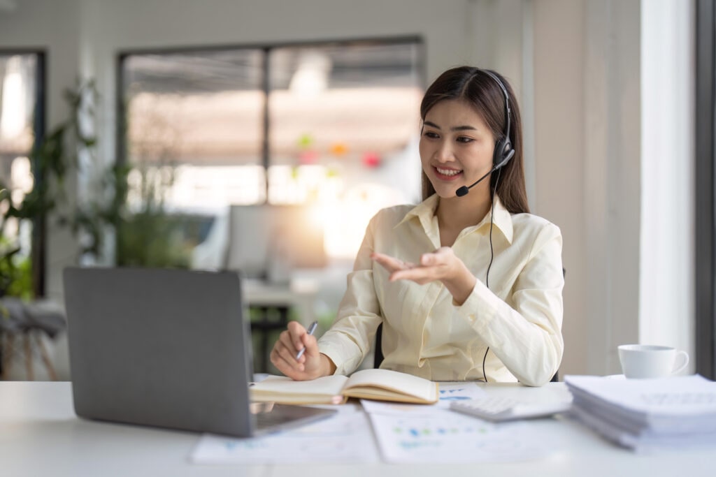 Portrait of happy smiling female customer support phone operator at workplace. Smiling beautiful Asian woman working in call center.