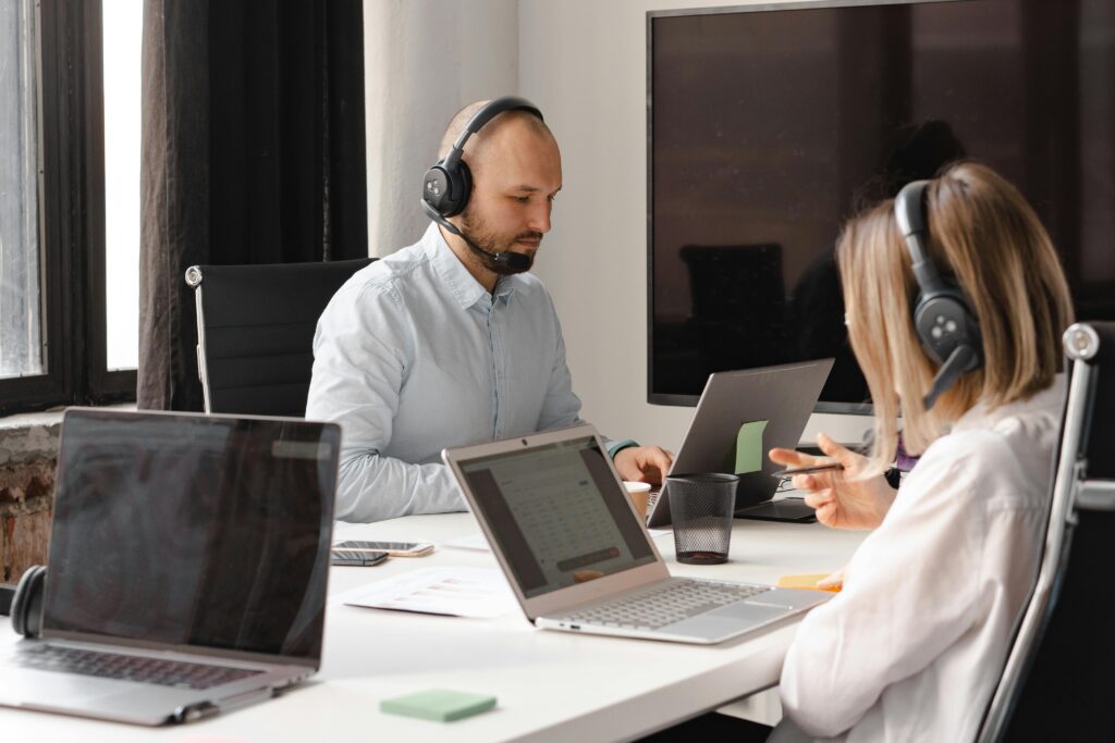 Two professionals collaborate at a desk, each using laptops for virtual receptionist tasks.